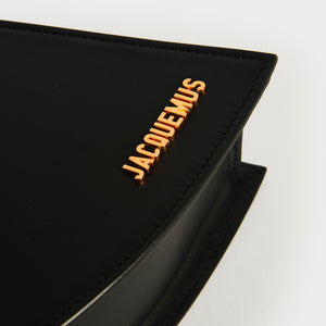 Close up shot of Jacquemus logo in gold hardware on La Vague shoulder bag in black leather.