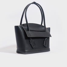 Load image into Gallery viewer, Side view of the BOTTEGA VENETA Arco Large Grained Leather Tote in Black with Gold Hardware
