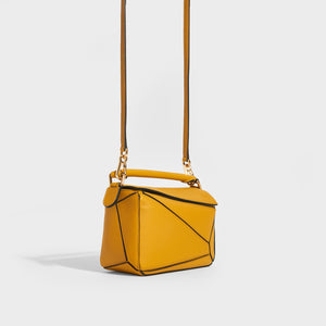 Side of the LOEWE Puzzle Mini Leather Shoulder Bag in Mustard with top handle and shoulder strap