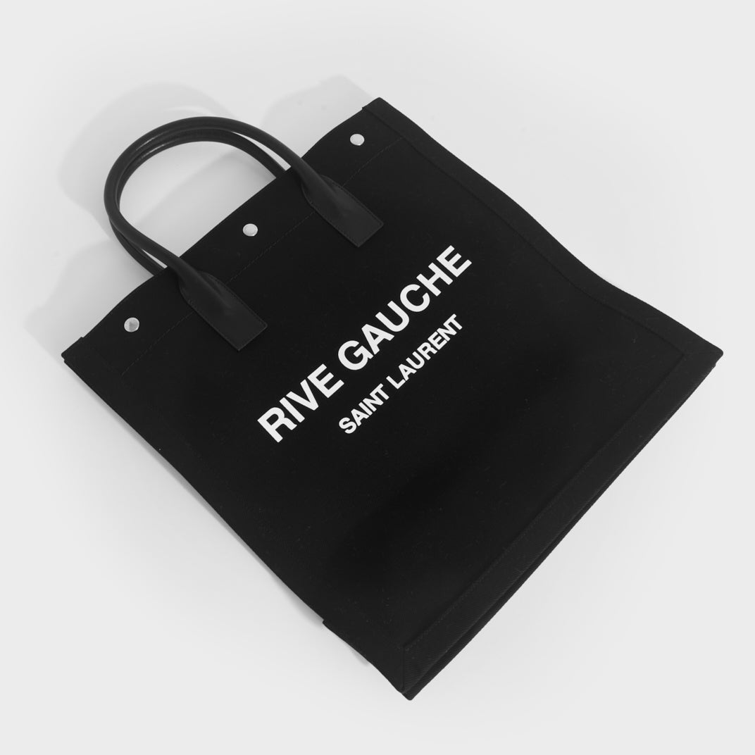 Flat shot of Saint Laurent Rive Gauche tote in black and canvas and white printed logo with black leather handles.