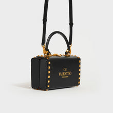 Load image into Gallery viewer, Side view of the VALENTINO Garavani Box Rockstud Alcove Leather Top Handle Bag in Black