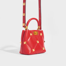 Load image into Gallery viewer, Side view of the VALENTINO Garavani Roman Stud Small Quilted Leather Tote in Red With Top Handle and Shoulder strap 