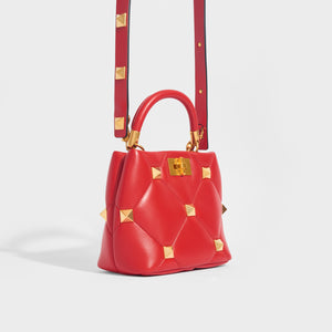Side view of the VALENTINO Garavani Roman Stud Small Quilted Leather Tote in Red With Top Handle and Shoulder strap 